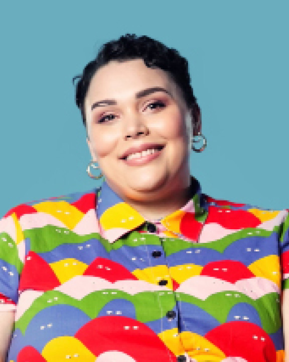 Cropped headshot of Sarah-Tai Black smiling in a colourful button-up.