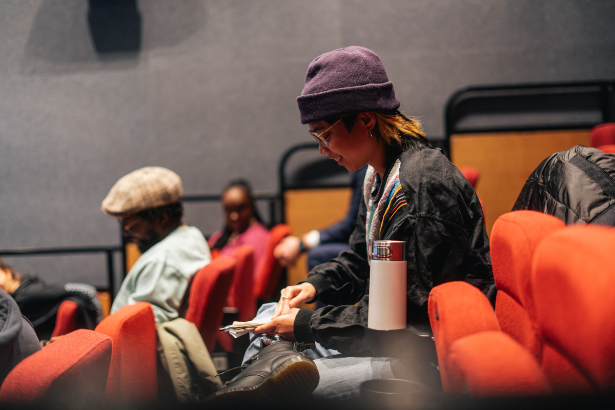 A former Fellow seated in a movie theatre and smiling at their notebook in their lap.